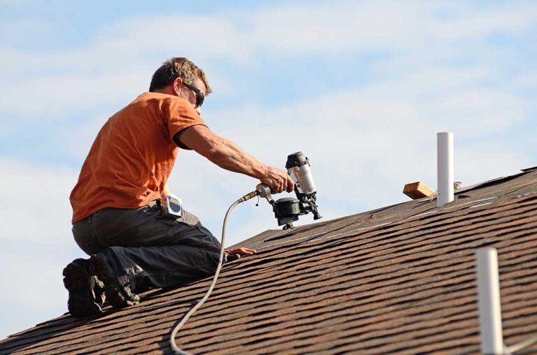 A person inspecting a pitched shingle roof for damage after a strong storm with scattered debris visible.