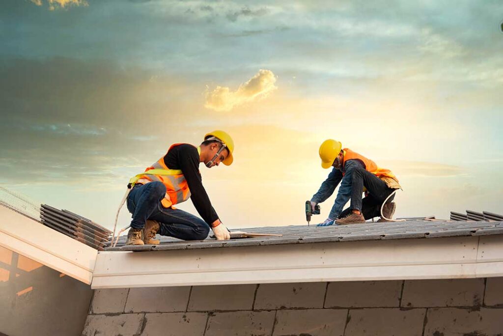 A worker applies a white protective coating across a low-slope roof with rollers and repair tools nearby.