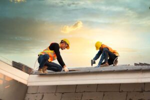 A worker applies a white protective coating across a low-slope roof with rollers and repair tools nearby.